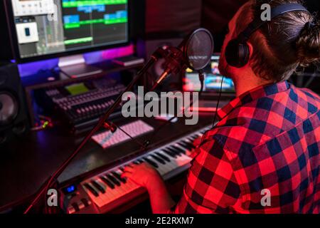 Le jeune homme blanc chante et enregistre une nouvelle piste dans le poste de travail de studio stéréo à l'aide d'un mélangeur de chansons et d'un microphone diffusé. Banque D'Images