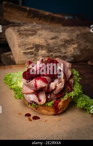 Hamburger artisanal démonté avec tranches de bacon frites et sauce aigre-douce et cerise sur le dessus, laitue fraîche avec pain de plomb à côté Banque D'Images