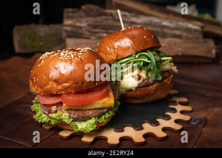 Deux délicieux hamburgers de bœuf frais servis avec des frites, l'un avec des noix frites et du fromage grillé sur une partie décorative en bois de mécanisme simple Banque D'Images