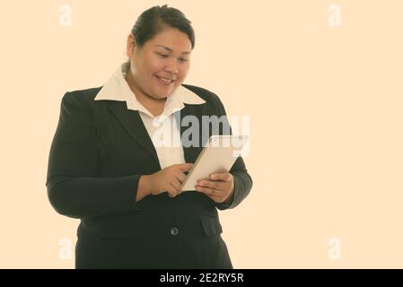 Studio shot of young happy fat Asian businesswoman smiling while using digital tablet Banque D'Images