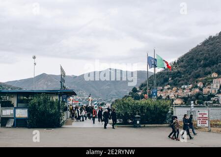 Como, région Lombardie, Italie - 14 janvier 2021 : touristes marchant dans le port du lac de Côme, quai du ferry dans la sombre journée d'hiver. Location de bateau pour les touristes Banque D'Images