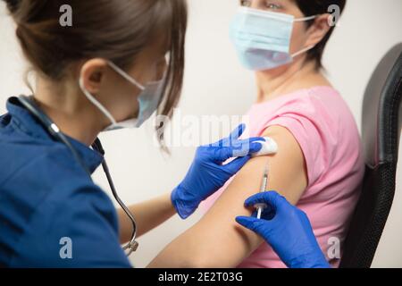 Épidémie. Fermez le médecin ou l'infirmière qui donne le vaccin au patient à l'aide de la seringue injectée. Fonctionne avec le masque facial. Protection contre le coronavirus, la pandémie COVID-19 et la pneumonie. Santé, médecine. Banque D'Images