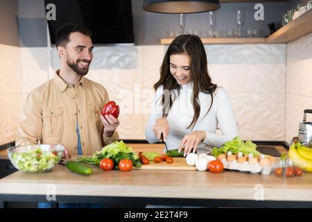 Un couple mignon passe du temps à cuisiner et semble heureux d'être ensemble dans la cuisine. Ils font de la salade avec des légumes frais et seulement des nutriti Banque D'Images