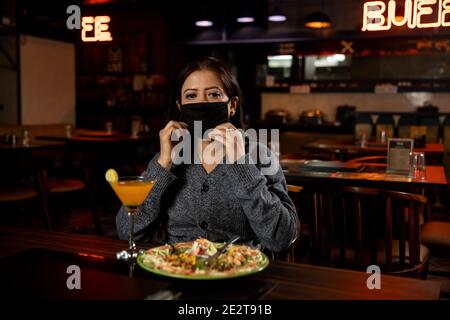 Portrait d'une femme portant un masque de protection du visage lorsqu'elle est assise dans un restaurant. Banque D'Images