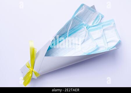 Un bouquet de masques jetables médicaux dans un emballage gris ultime avec un noeud lumineux. Le concept de l'essentiel pendant une pandémie. Banque D'Images