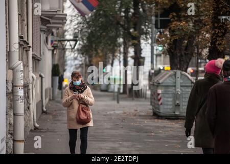 BELGRADE, SERBIE - 29 NOVEMBRE 2020: Jeune femme portant un masque respiratoire vérifiant des applications sur son smartphone dans la rue de Belgrade, pendant le Th Banque D'Images