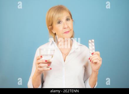 femme âgée avec un verre d'eau et des pilules sur bleu arrière-plan Banque D'Images