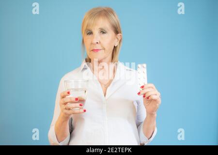 femme âgée avec un verre d'eau et des pilules sur bleu arrière-plan Banque D'Images