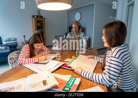 Homeschooling, pendant le verrouillage de janvier 2021, les enfants étudiant à la maison pour l'école, leur mère dans le bureau à domicile travaillant sur l'ordinateur portable avec vide Banque D'Images