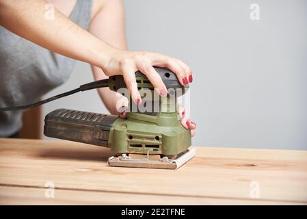 Travail de menuiserie, détail d'une jeune femme caucasienne avec ses ongles fait le ponçage du bois, à l'aide d'une ponceuse électrique. Banque D'Images