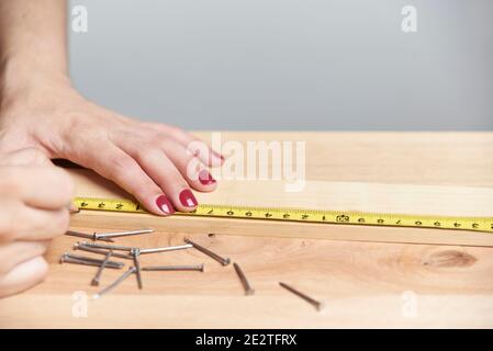 Détail d'une jeune femme travaillant en charpenterie, marquant les mesures sur une bande de bois avec un crayon. Menuisier femelle avec mains avec vernis à ongles. Banque D'Images