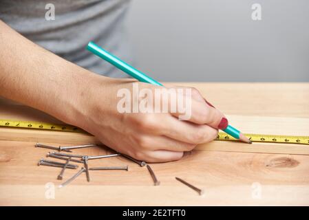 Détail d'une jeune femme travaillant en charpenterie, marquant les mesures sur une bande de bois avec un crayon. Banque D'Images