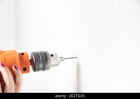 Femme avec une perceuse à percussion forant un mur blanc. Image détaillée avec espace de copie. Banque D'Images
