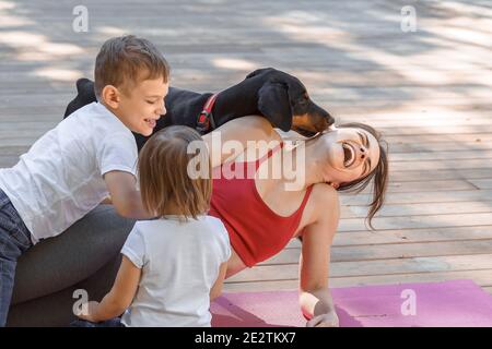 Jeune belle mère avec bébé fils, fille et avec chien faisant de l'exercice et faisant du yoga au parc d'été au lever du soleil. La maternité sportive et saine. Fern