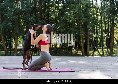 Jeune belle femme faisant le yoga pose dans le parc avec le chien doberman. Émotions positives et la santé de communiquer avec un animal de compagnie et des sports Banque D'Images
