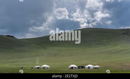 Bayan Olgi, Mongolie, 5 août 2019 : cinq yourtes avec voitures dans la steppe de Mongolie avec montagnes, collines et nuages sombres. Banque D'Images