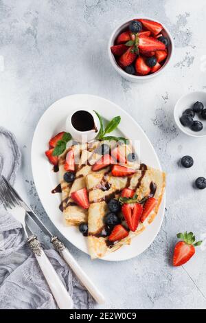 Crêpes françaises maison en crêpe Suzette avec sauce au chocolat, fraises fraîches et miel pour le petit déjeuner dans une assiette en céramique blanche. Espace pour le texte ou la recette Banque D'Images