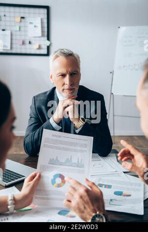 Investisseur mature regardant des partenaires commerciaux avec des documents sur flou premier plan Banque D'Images