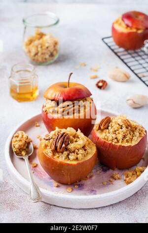 Quatre pommes cuites au four rouge farcies de noix de pacanes, de cannelle, de strayzel et de miel sur fond clair de béton ancien. Dessert d'automne ou d'hiver. Foyer sélectif Banque D'Images