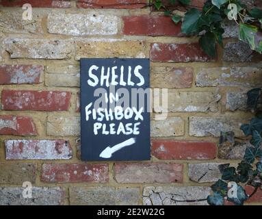 Panneau d'instructions sur le mur de briques indiquant de laisser les coquilles dedans boîte à poissons Banque D'Images