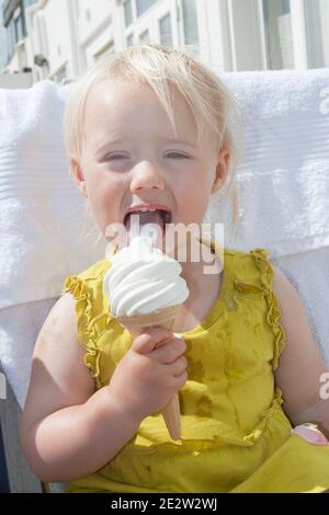 Une jeune fille blonde heureuse de 3 ans léchant un Glace en été au bord de la mer aux Etats-Unis Royaume Banque D'Images