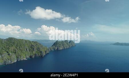 Vue aérienne des îles vallonnées sur la côte bleue de l'océan. Personne de paysage de la nature de Palawan, El Nido Isles, Philippines. Forêt tropicale verte à la montagne s'étend sous des nuages moelleux sur le ciel. Tir de drone cinématographique Banque D'Images