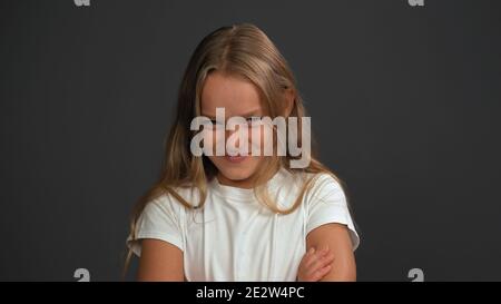 Gros plan. Petite fille de 8,10 ans avec les mains repliées regarde en question l'appareil photo portant t shirt blanc isolé sur gris foncé ou noir Banque D'Images