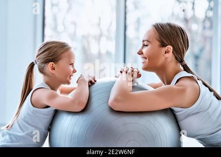 Un coup de main de belle jeune mère est assis avec sa fille sur le sol de la balle de taille maigre à la salle de gym. Concept familial sportif Banque D'Images