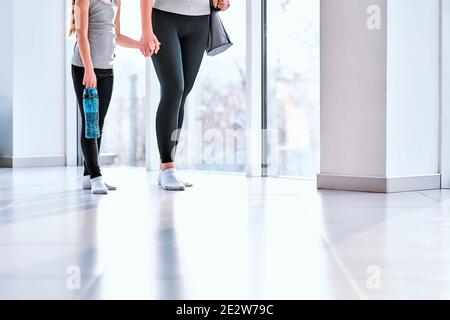 Jeune femme souriante et petite belle fille avec sac de sport et une bouteille d'eau portant des vêtements de sport et bavardant pendant la marche centre de fitness Banque D'Images