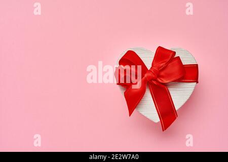 Boîte cadeau en forme de coeur avec un ruban rouge sur fond rose. Carte postale concept de la Saint-Valentin. Vue de dessus. Banque D'Images