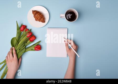 Tasse de café, croissant, bloc-notes, stylo, téléphone et fleurs Banque D'Images