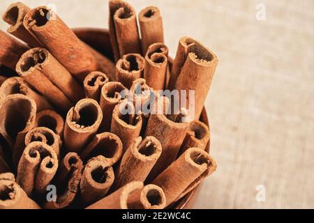 Gros plan - tas de bâtons d'écorce de cannelle dans une tasse en bois sur la nappe en lin. Banque D'Images