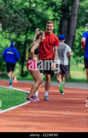 Un jeune couple s'étire avant de commencer sa routine de jogging matinale sur une piste de tartan au parc. Banque D'Images