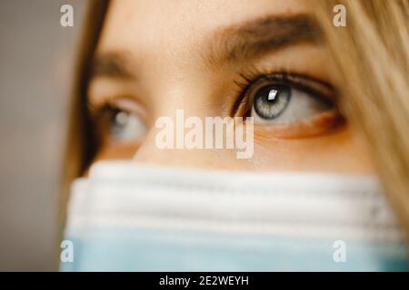 Vue macro: Belle jeune femme avec des yeux bleus portant un masque médical et regardant loin Banque D'Images