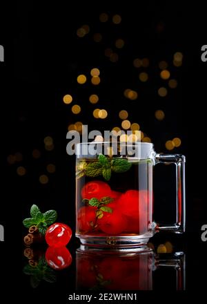 Thé chaud à la cerise avec cannelle et menthe dans une tasse en verre sur table miroir et arrière-plan noir Banque D'Images