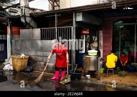 Femme en bottes roses nettoie la rue devant Talat Boutique noi à Bangko Banque D'Images