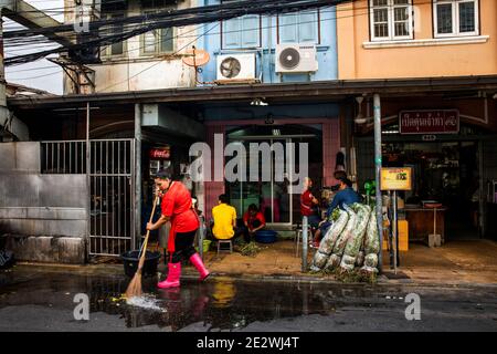 Femme en bottes roses nettoie la rue devant Talat Noi Garden Shop Banque D'Images