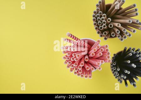 Tubes à boire rouge et marron en papier et fécule de maïs, matériau biodégradable et verres en papier écologique sur fond jaune et gris tendance couleur 2021 Banque D'Images