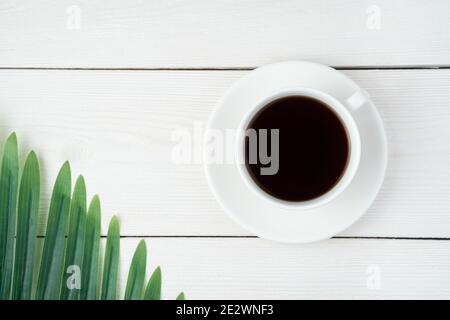 Tasse à café blanche en céramique sur fond blanc flou avec branche de paume. Banque D'Images