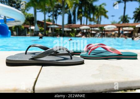 Deux paires de pantoufles au bord de la piscine par temps ensoleillé. Banque D'Images