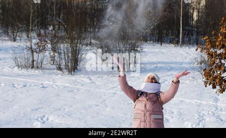 Femme vêtue d'hiver lors d'une promenade dans le parc. Jette une poignée de neige. Il y a beaucoup de neige autour. Banque D'Images