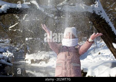 Femme vêtue d'hiver lors d'une promenade dans le parc. Jette une poignée de neige. Une rivière coule à proximité. Il y a beaucoup de neige autour. Banque D'Images