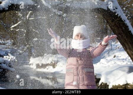 Femme vêtue d'hiver lors d'une promenade dans le parc. Jette une poignée de neige. Une rivière coule à proximité. Il y a beaucoup de neige autour. Banque D'Images