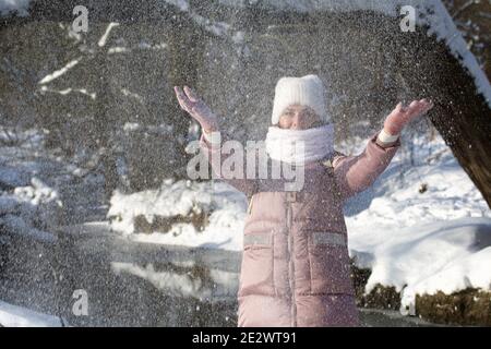 Femme vêtue d'hiver lors d'une promenade dans le parc. Jette une poignée de neige. Une rivière coule à proximité. Il y a beaucoup de neige autour. Banque D'Images