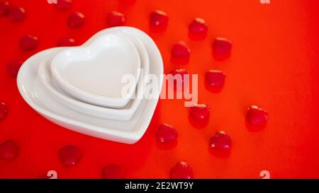 Le cœur forme des plaques blanches sur fond rouge avec de petits bonbons - concept de jour de Saint Valentin Banque D'Images