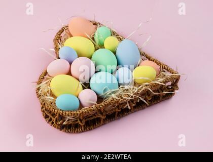 Oeufs de Pâques multicolores pastel dans un panier en forme de coeur sur fond rose. Vue de dessus, placer pour le texte. Carte de vœux. Banque D'Images