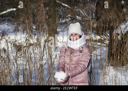 Femme vêtue d'hiver lors d'une promenade dans le parc. Jette une poignée de neige. Il y a beaucoup de neige autour. Banque D'Images