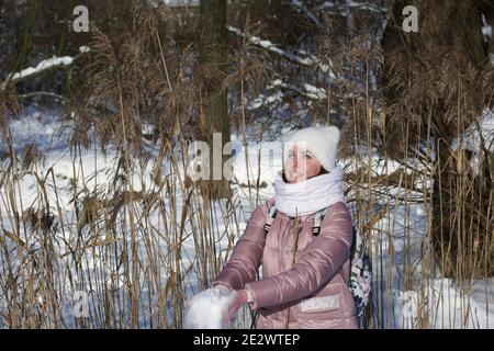 Femme vêtue d'hiver lors d'une promenade dans le parc. Jette une poignée de neige. Il y a beaucoup de neige autour. Banque D'Images