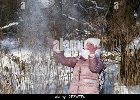 Femme vêtue d'hiver lors d'une promenade dans le parc. Jette une poignée de neige. Il y a beaucoup de neige autour. Banque D'Images