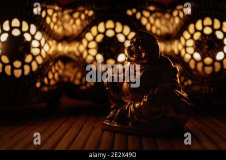 Figurine Golden Laughing Buddha avec des bougies complexes créant des ombres chaudes et méditatives Banque D'Images